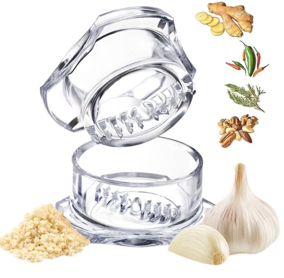 A clear plastic garlic press sits open with chopped garlic, garlic bulbs, ginger, nuts, herbs, and peppers nearby—perfect for prepping ingredients like fresh garlic for instant pot mashed potatoes.